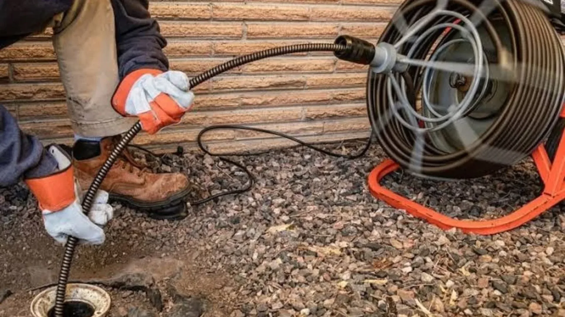 Plumber feeding a drain machine cable from a reel at an outdoor sewer cleanout